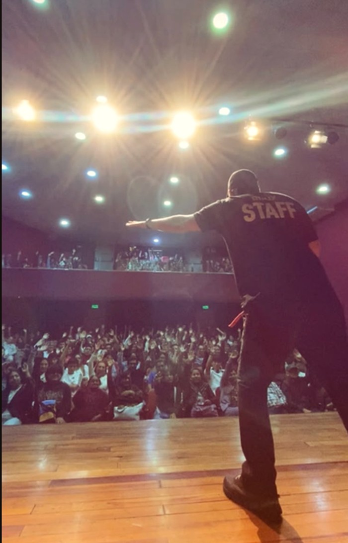 Equipo de producción con polo de staff, de espaldas, frente a la sala llena antes de que empiece el show.
